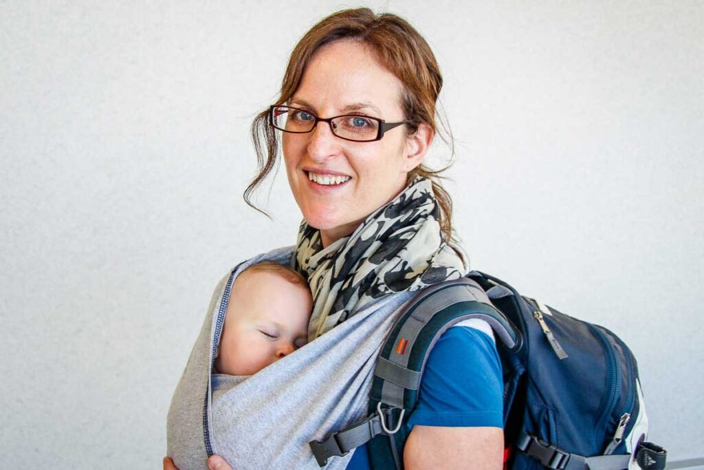 BabyCanTravel.com owner Celine Brewer, carries a sleeping baby in a Baby K'Tan carrier in an airport before flying with a baby.