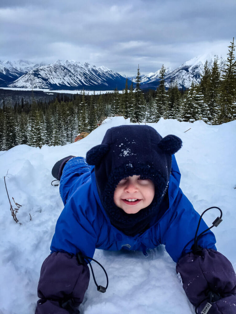 A warmly dressed toddler plays in the snow while on a winter hike with his family in the Canadian Rocky Mountains.