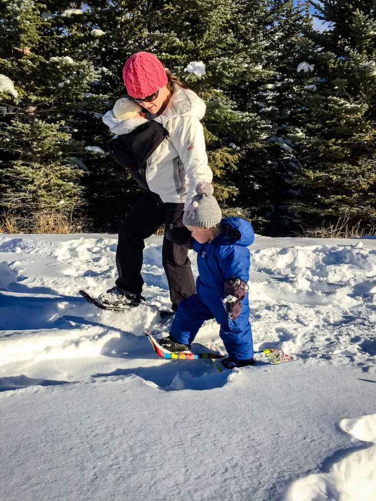 Celine Brewer, owner of BabyCanTravel.com, takes her toddler snowshoeing, while baby-carrying her infant.