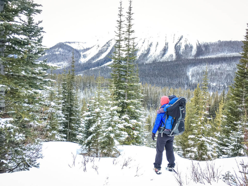 Celine Brewer is snowshoeing with a baby in a backpack carrier.