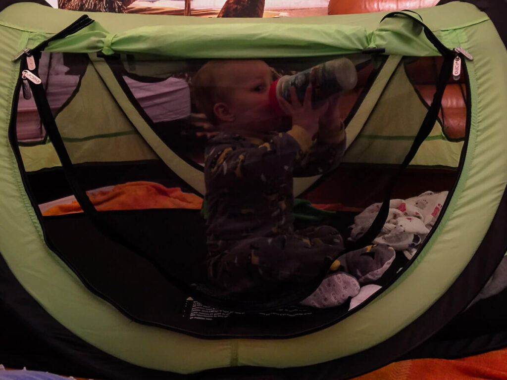 toddler sitting up in KidCo PeaPod Plus portable bed for toddlers.