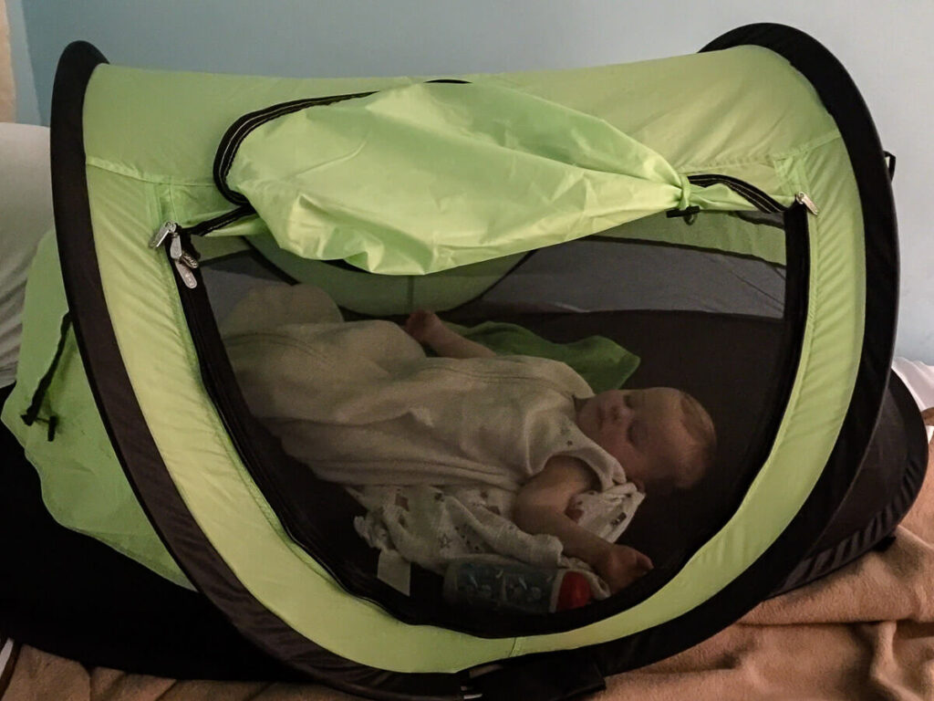 a baby sleeping in KidCo PeaPod Plus travel bed