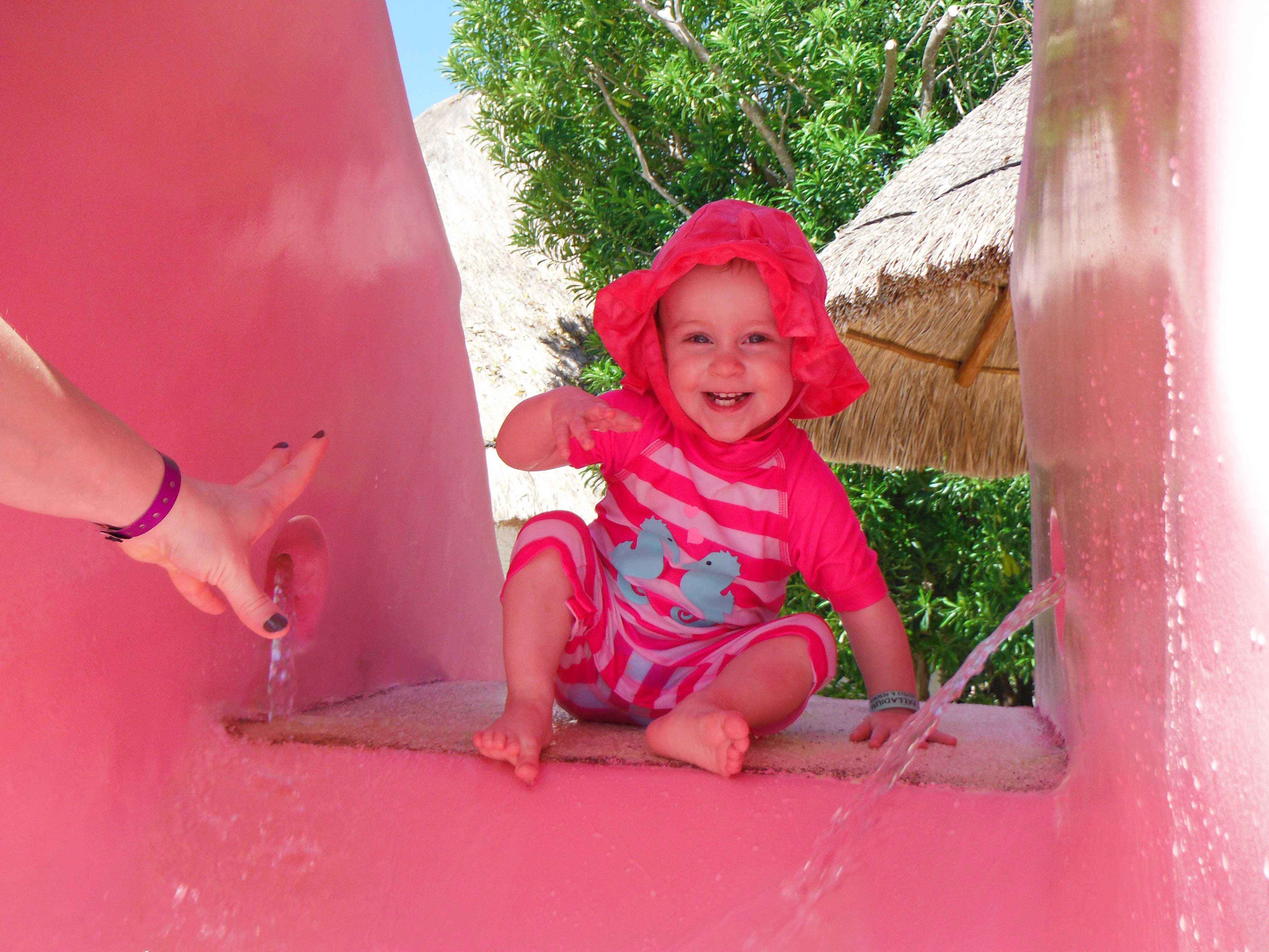 a baby girl plays on a water slide at a family vacation to an all-inclusive resort in Mexico.
