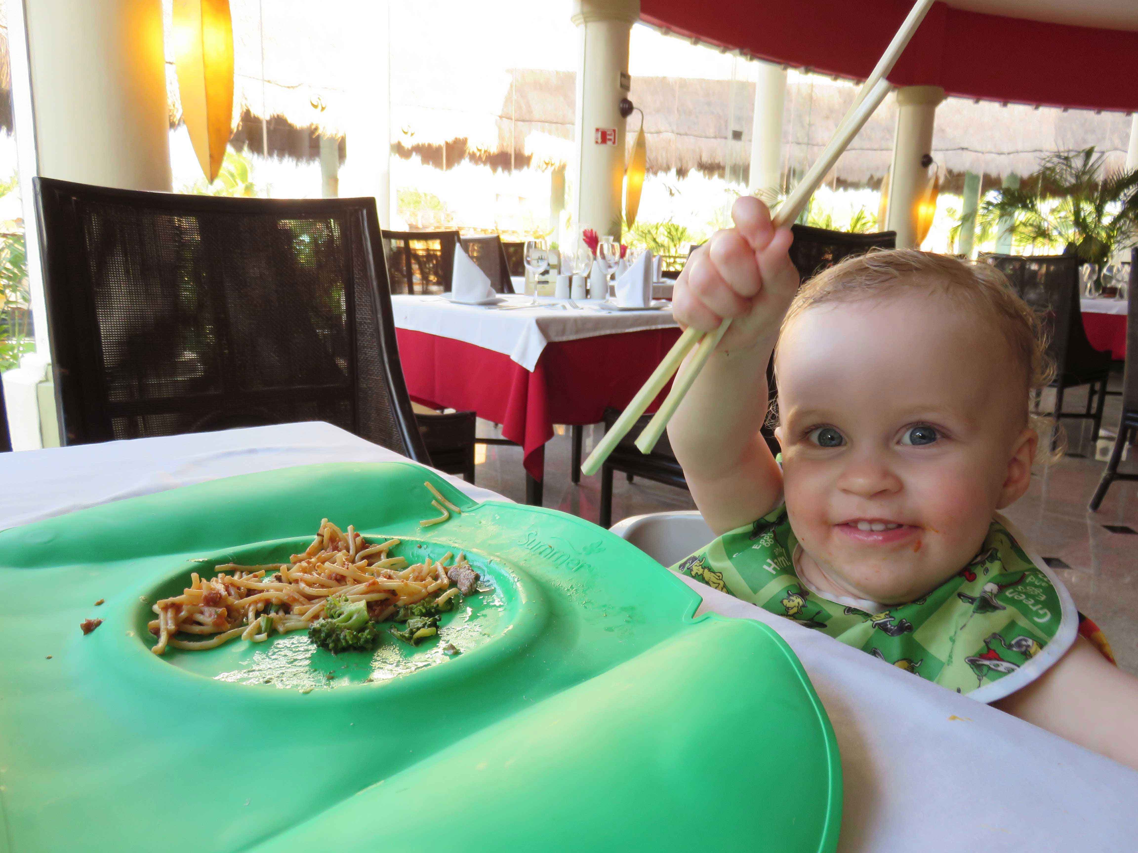 a happy baby holds chopsticks at a restaurant at a baby-friendly all-inclusive resort in Mexico.