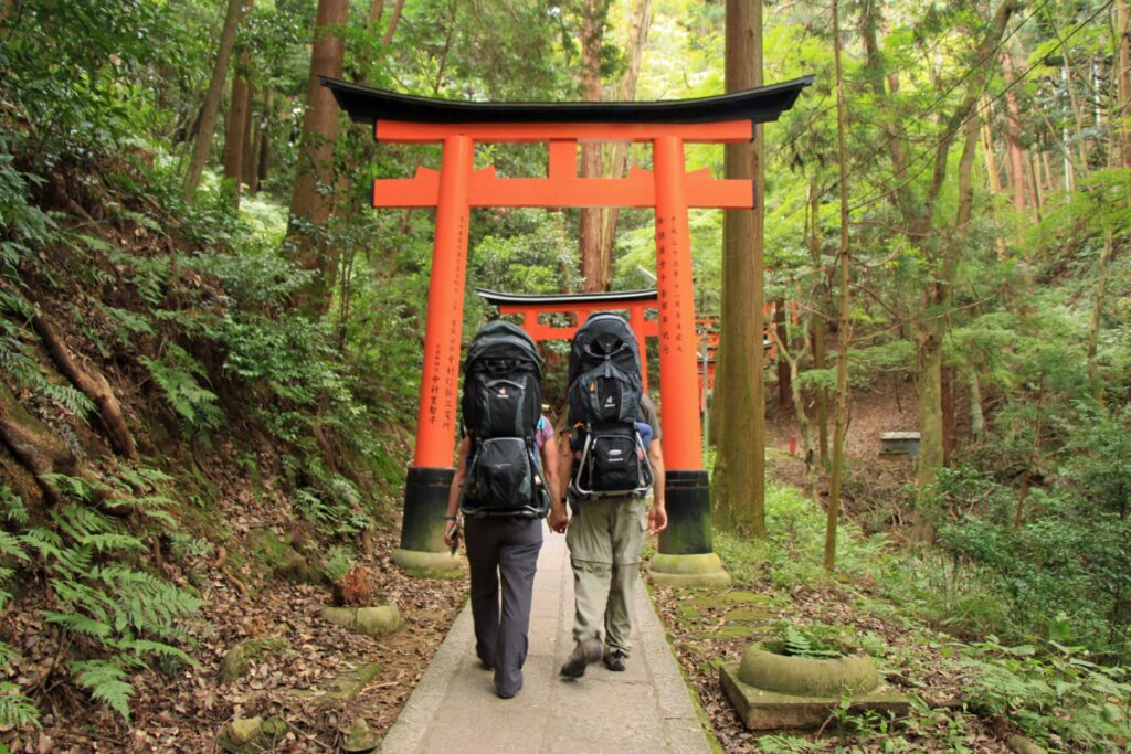 Two parents hike the Fushimi Inari Hike in Japan with their children in toddler hiking backpack carriers.