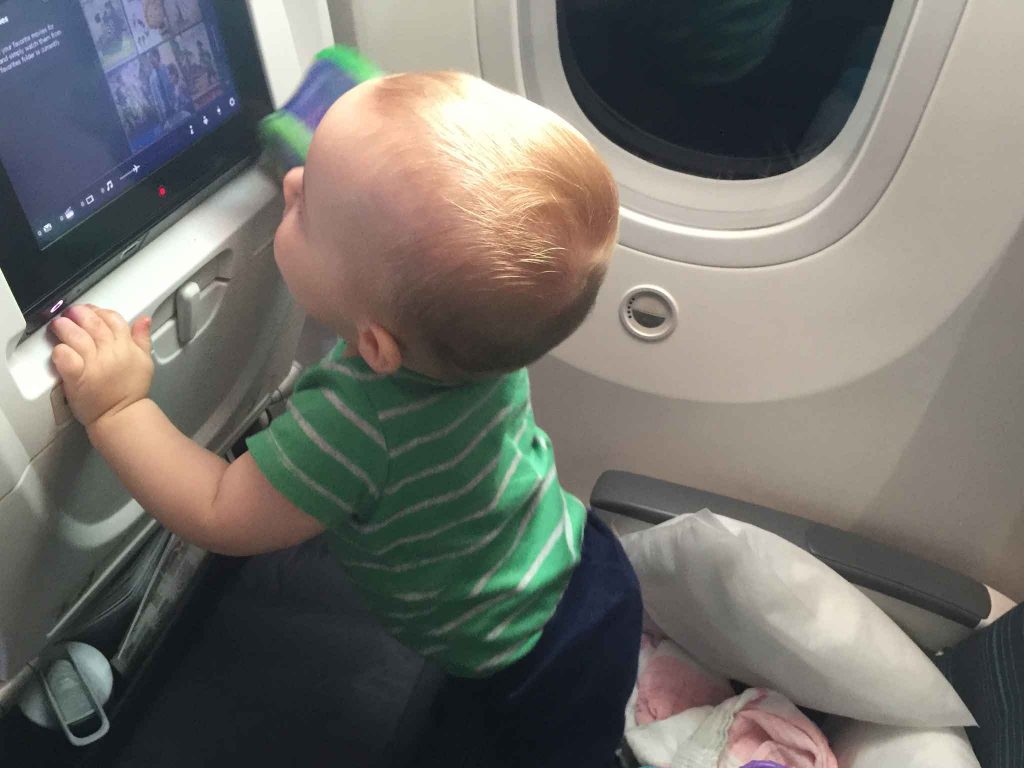 a toddler from BabyCanTravel.com plays with the seat-back tv screen on a family flight.