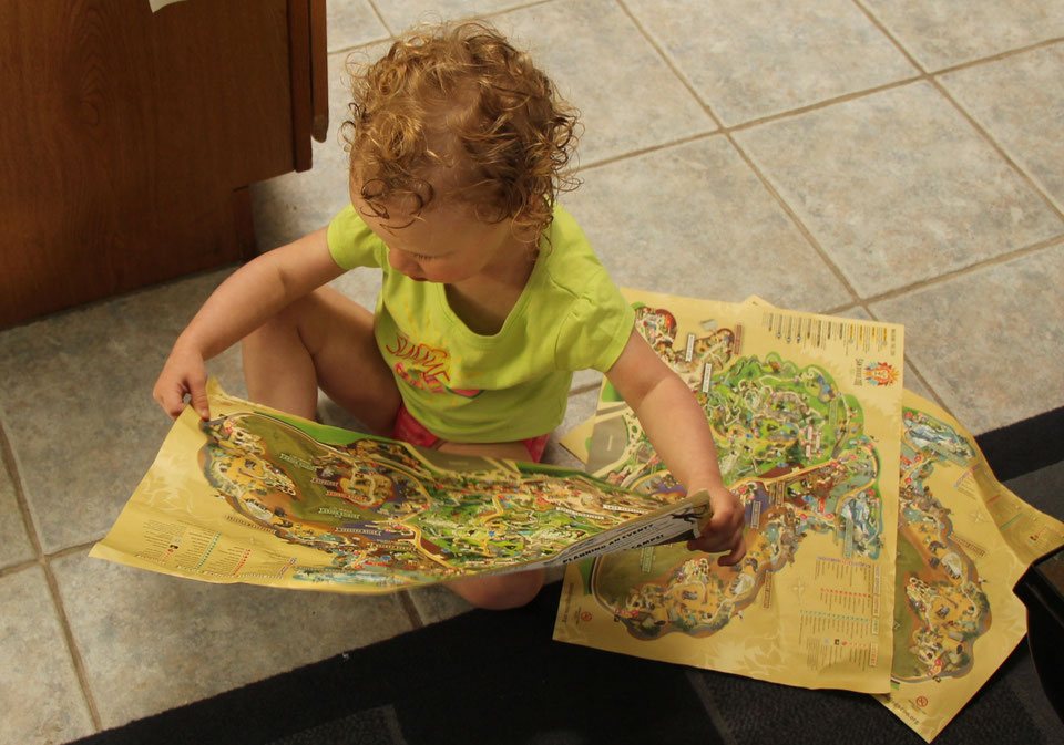 A toddler enjoys looking at a paper copy of the San Diego zoo map, with several more scattered on the ground.