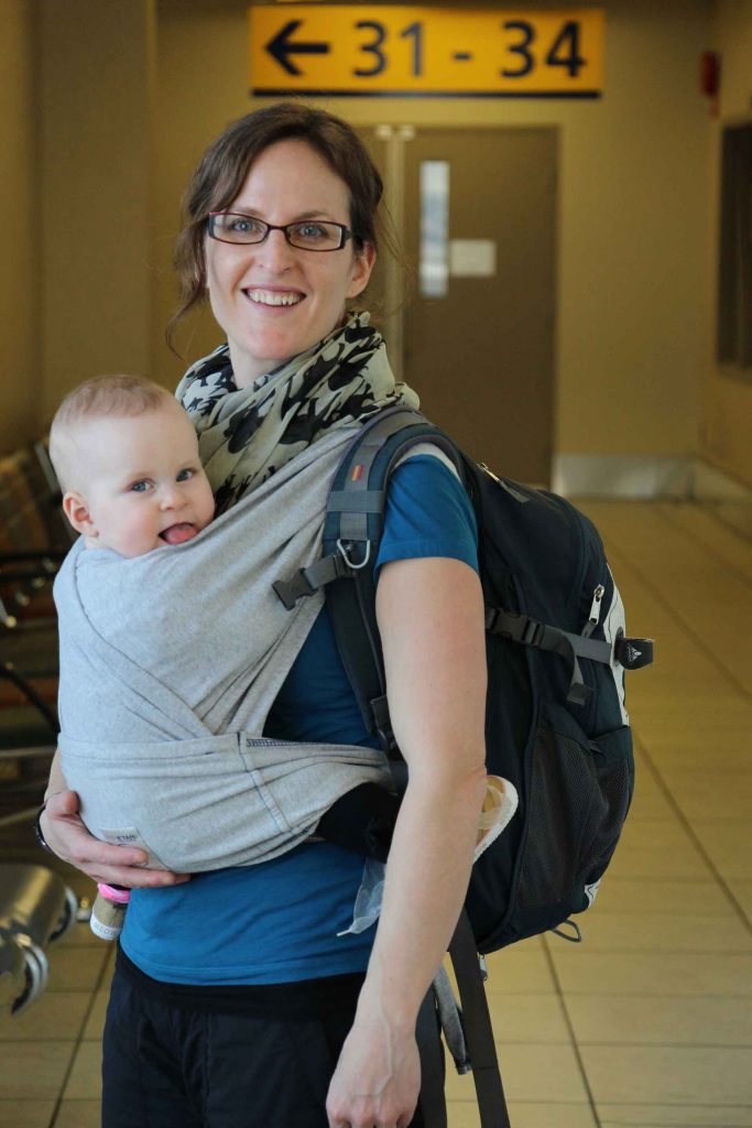 a mother navigates the airport by carrying her baby in a carrier before her family flight to a baby friendly destination.