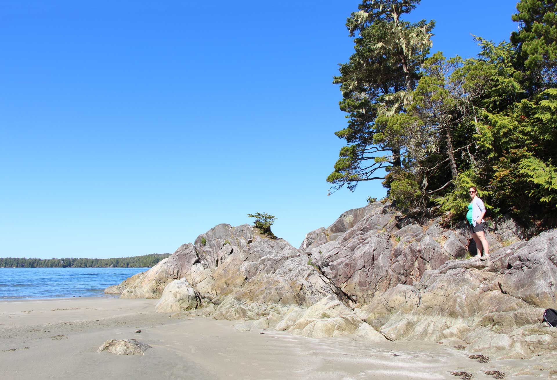 a pregnant woman stands on the beach in Tofino, BC during her babymoon vacation.