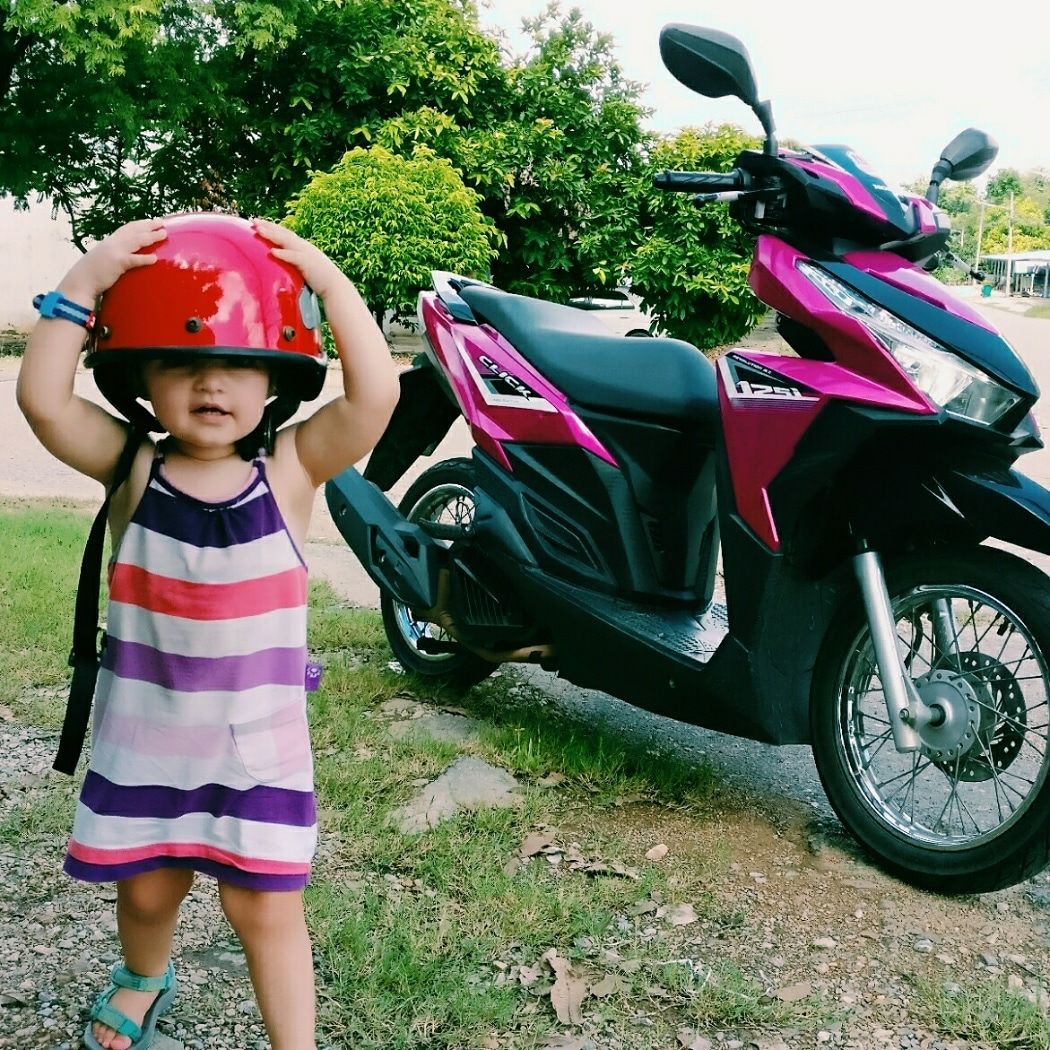 a two year old tries on a moped helmet while on a family vacation.