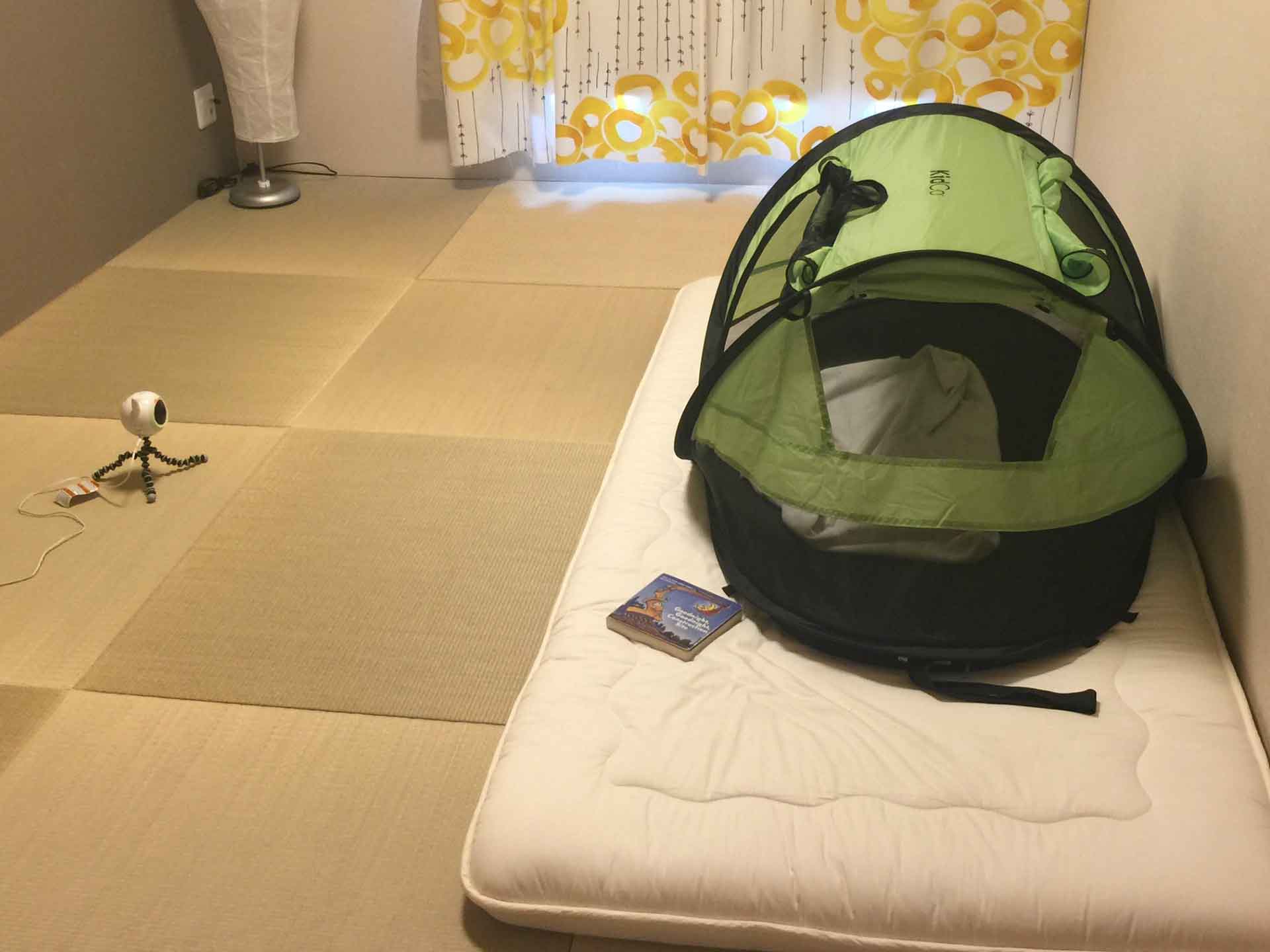 a child from the BabyCanTravel.com family, sleeps in a KidCo PeaPod Plus Travel Tent with a baby monitor watching.