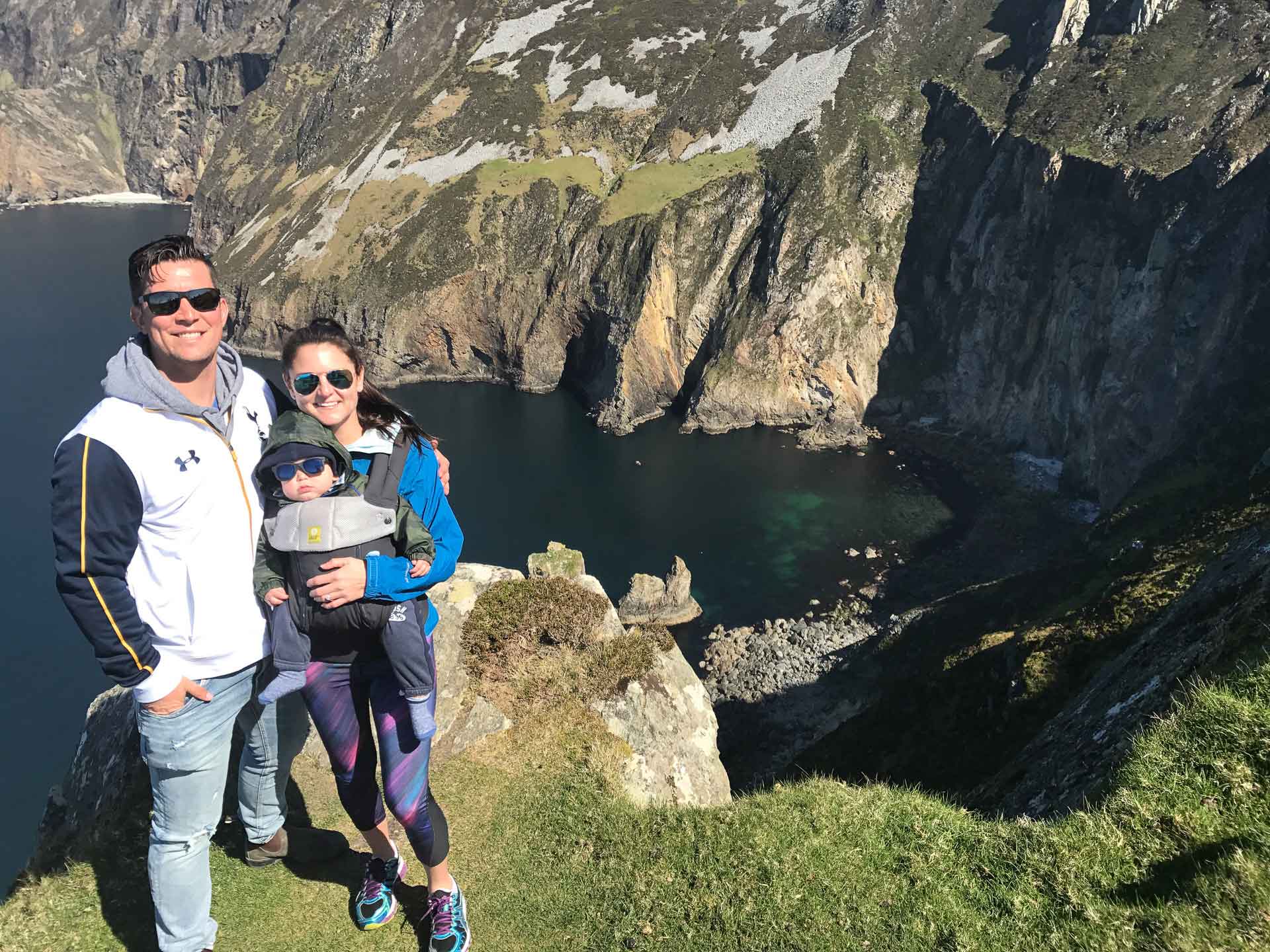 a proud mother and father pose with their baby while on a family vacation near the ocean.