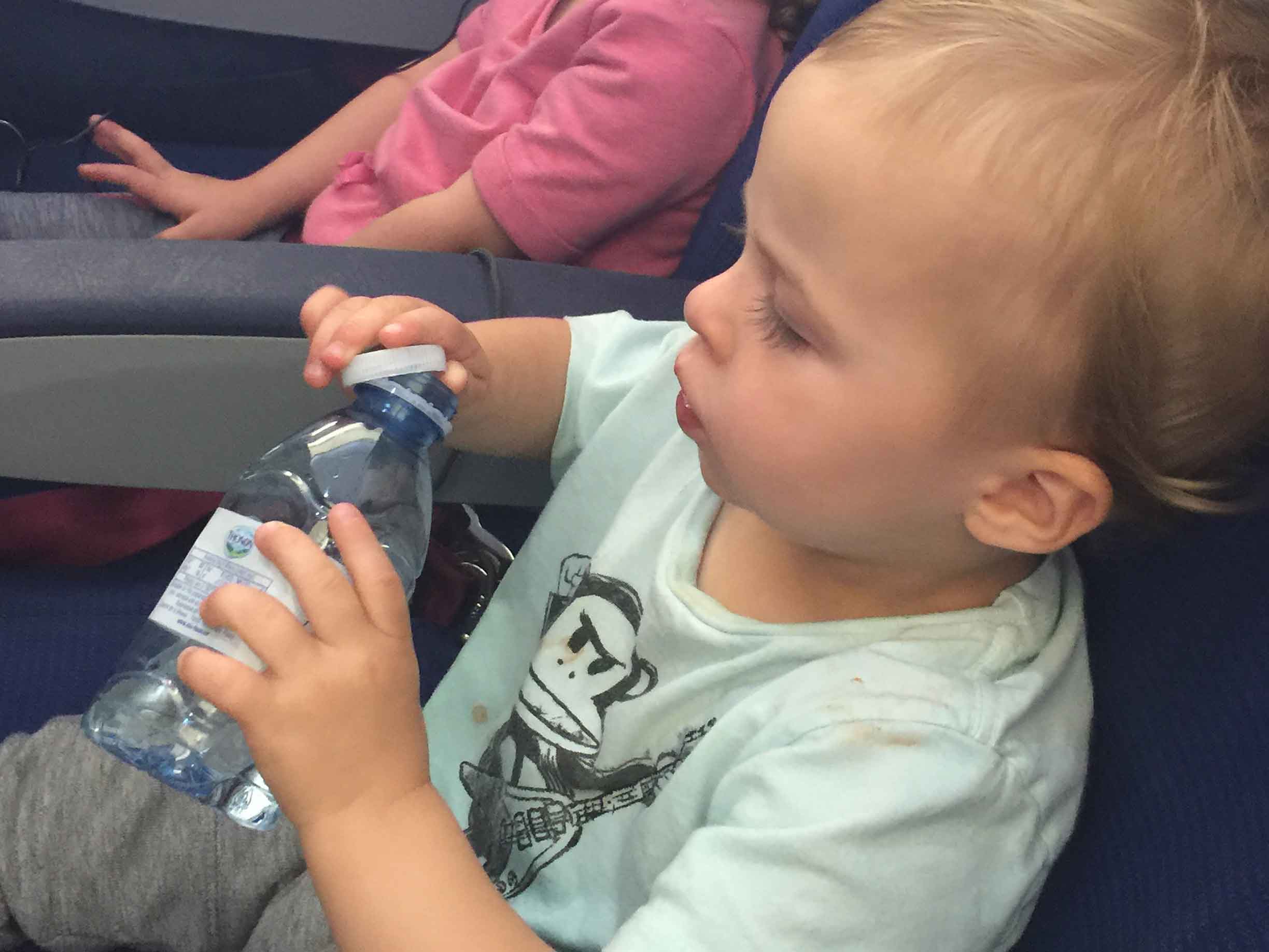 a toddler plays with an empty water bottle and cap on a family flight.