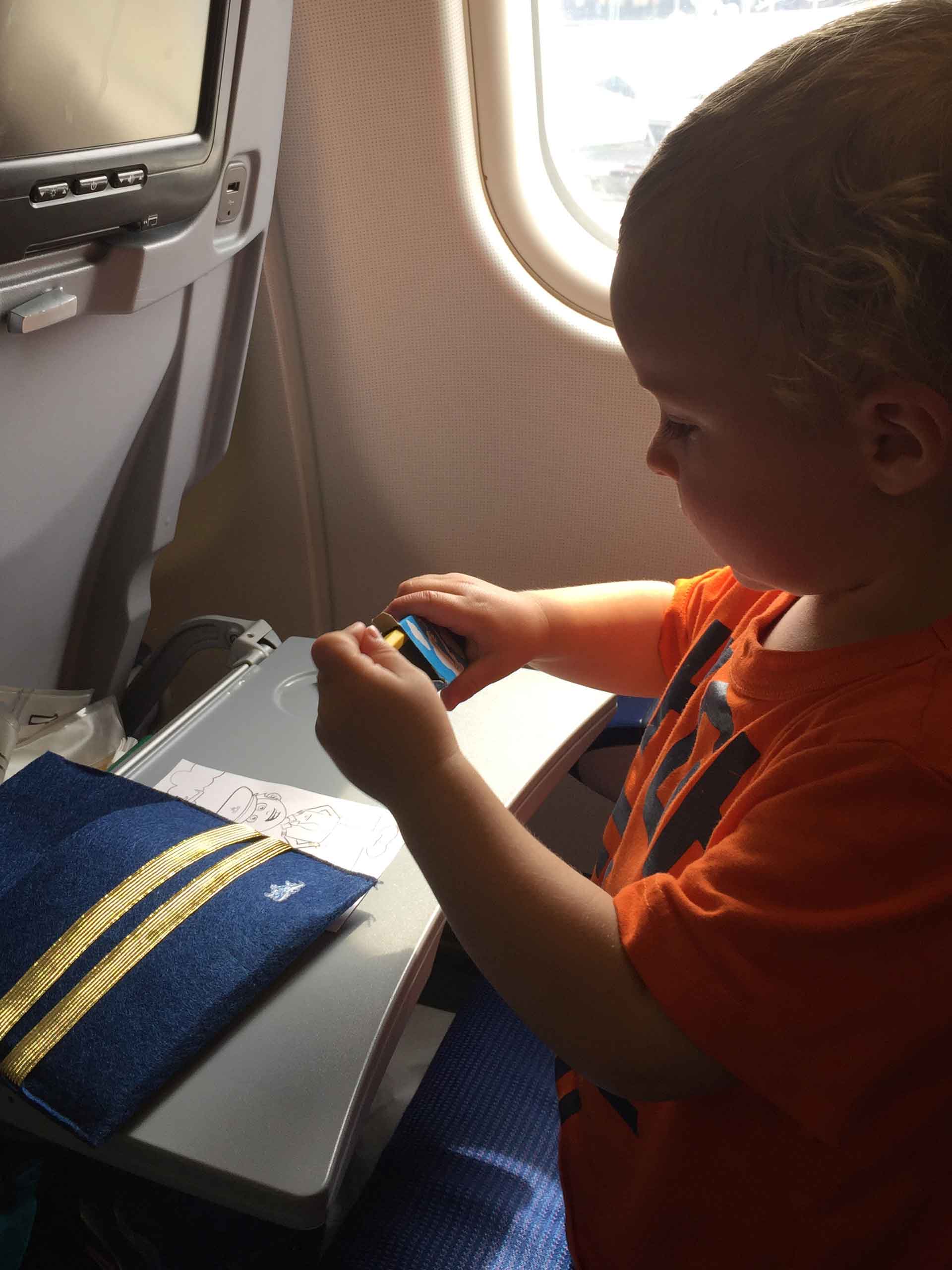 a toddler is entertained by the kids activity book provided by the airline for his long haul flight.