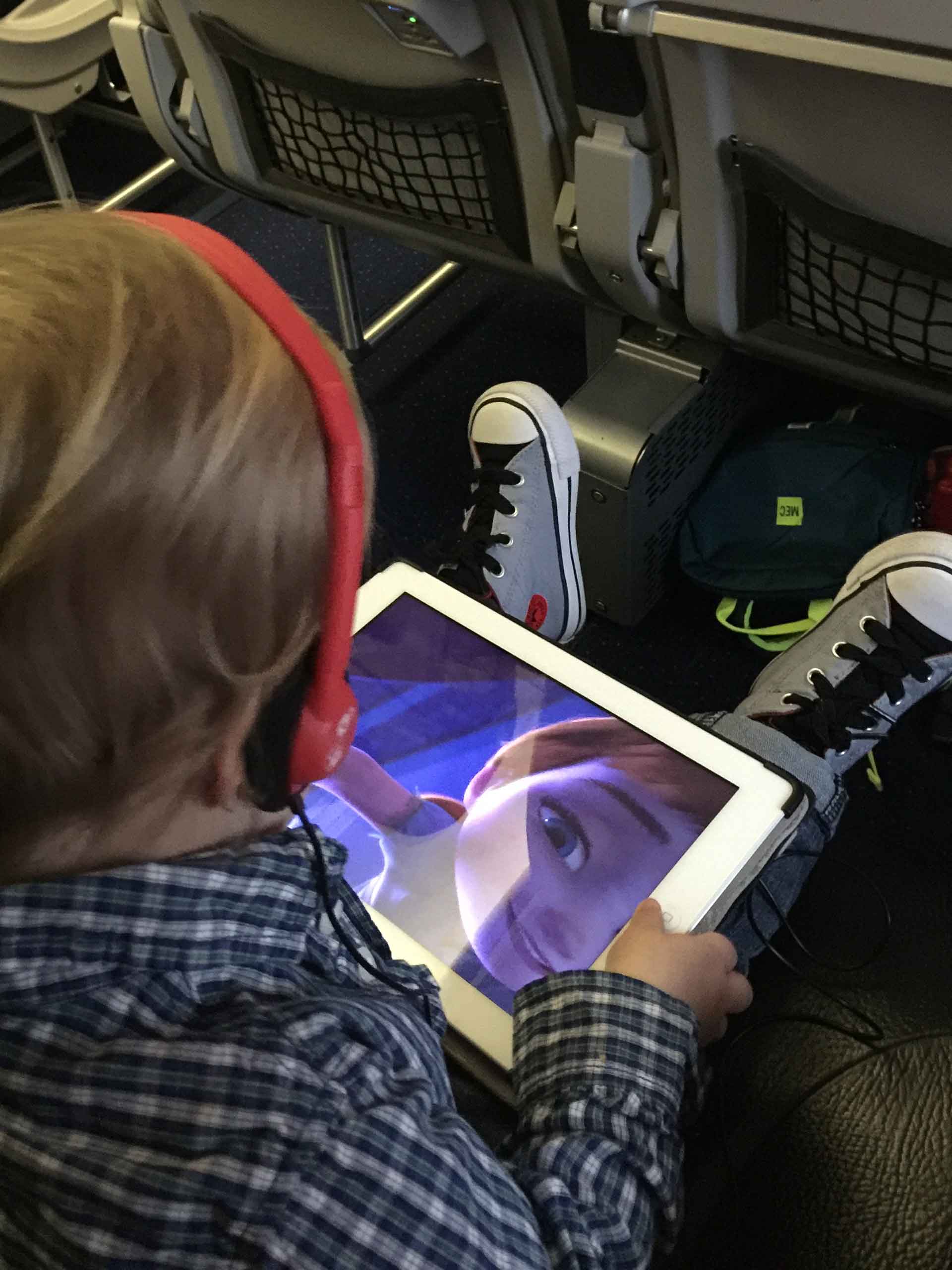 a toddler on an airplane watches Frozen on an iPad.