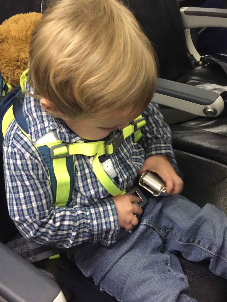 A toddler buckles his seatbelt as he board a flight for a family trip.