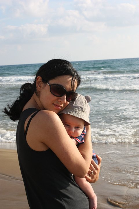 a mother cuddles her baby near the beach on a family vacation.