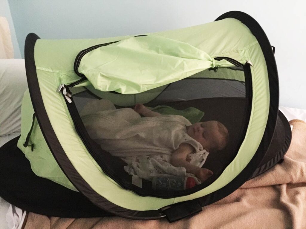 a toddler from BabyCanTravel.com is fast asleep in a KidCo PeaPod Plustent on a family vacation.