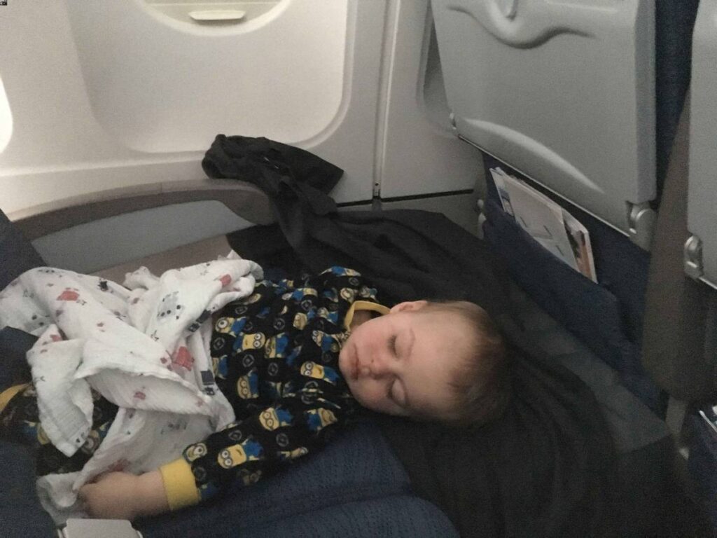 a toddler asleep on a long flight using an inflatable airplane bed