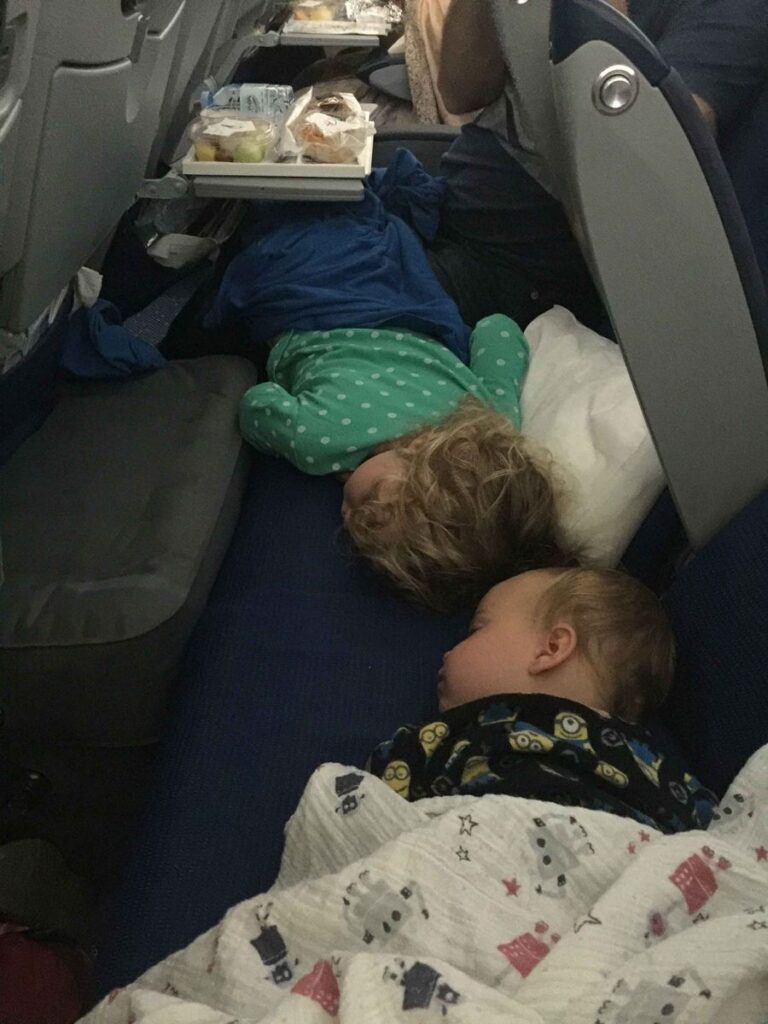 Two young kids sleep on a plane using Fly Tots