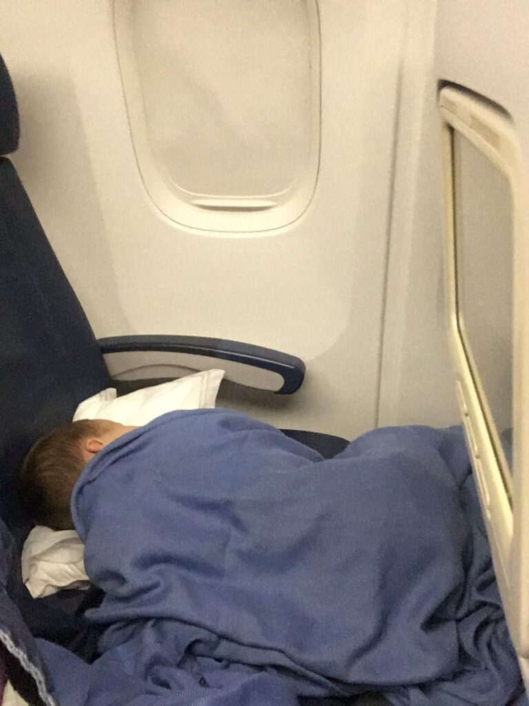 a young boy sleeps soundly on a red eye flight to Asia