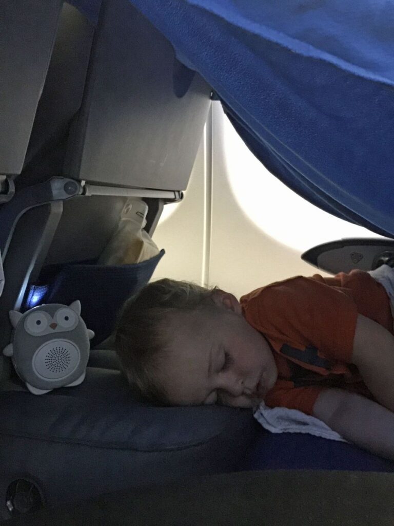 a boy sleeps on a red eye flight to Europe on a Fly Tot airplane bed for toddlers.