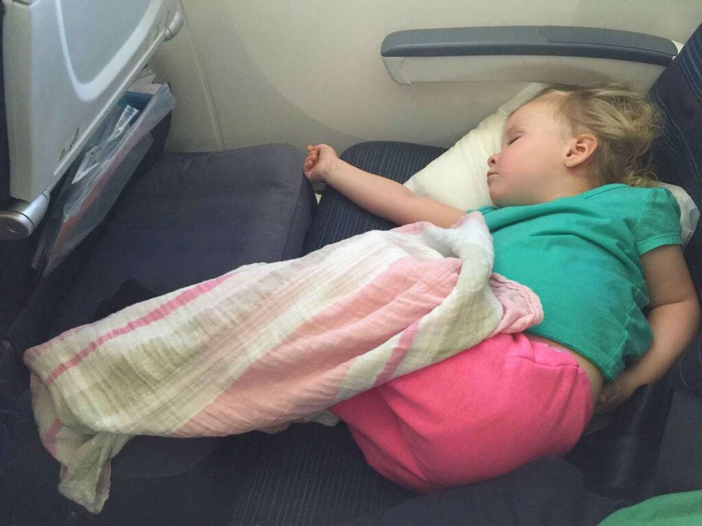 a preschooler sleeps comfortably on a long flight using an Original Fly tot airplane cushion