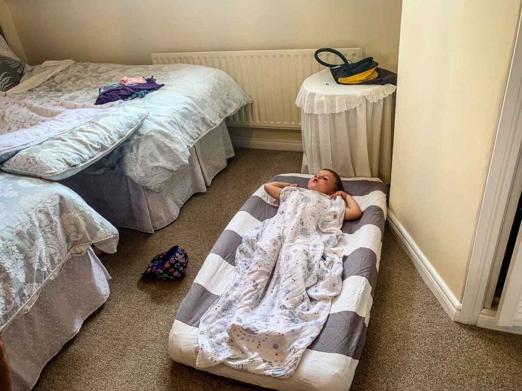 A BabyCanTravel.com toddler sleeps on a Shrunks inflatable toddler travel bed in a small European hotel room.