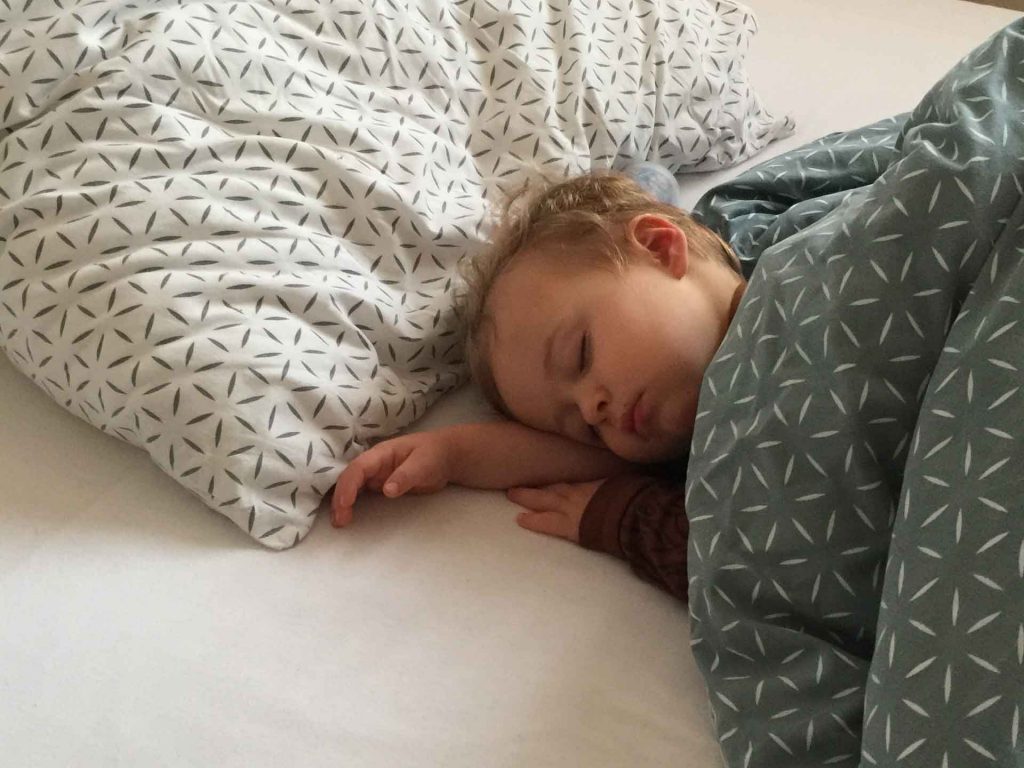 a toddler sleeps on a hotel bed while on a family vacation.