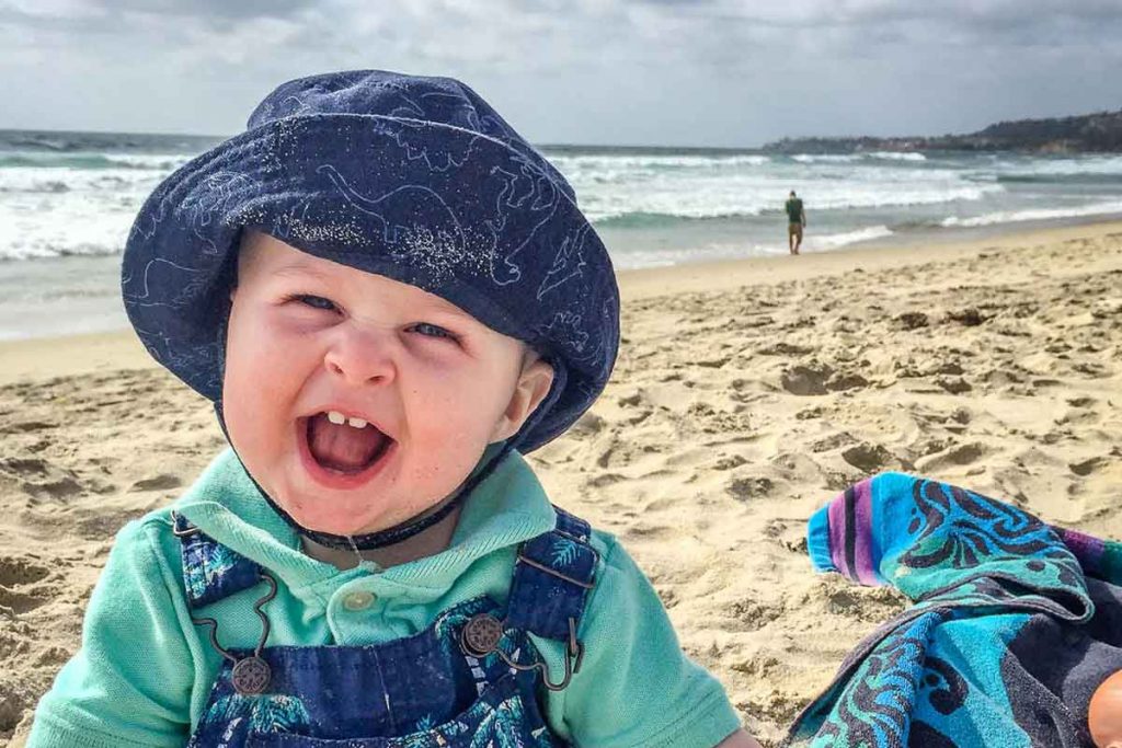 a happy baby on the sand shows why beaches make some of the best holiday destinations with a baby.