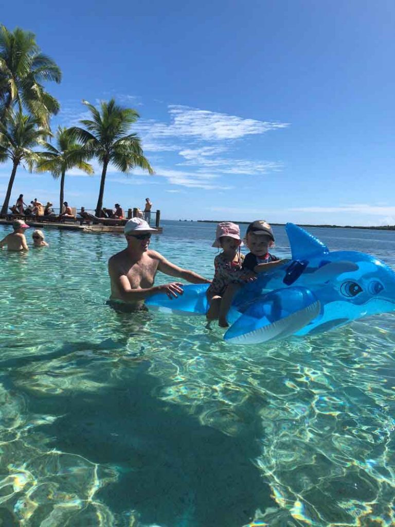 a dad gives his children a ride on an inflatable dolphin while on a family vacation to Fiji - one of the best baby friendly destinations in Oceania.