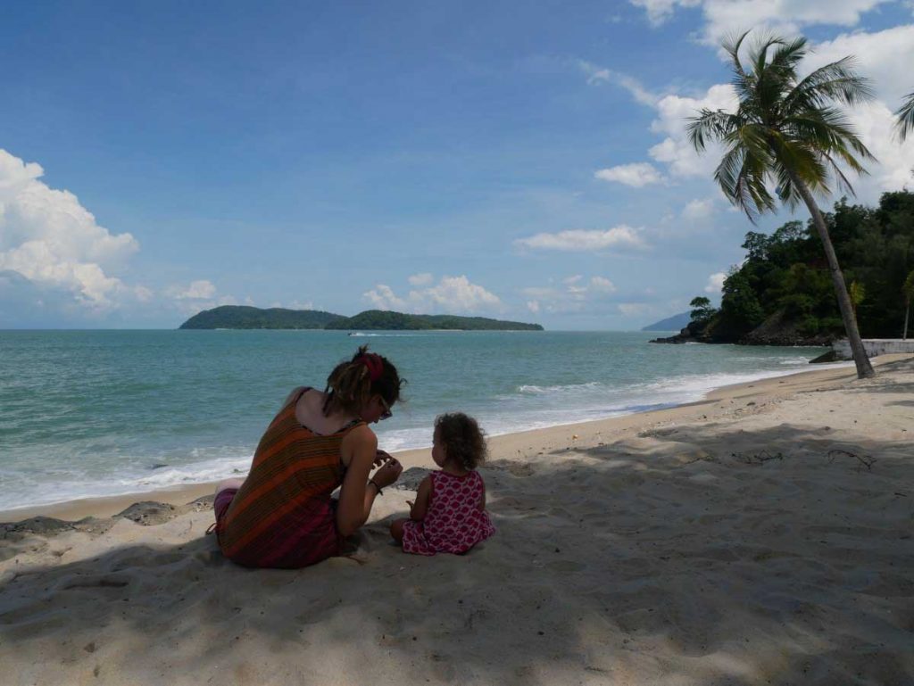 a mother and her 1 year old look at seashells on the beach while on a family trip to Malaysia
