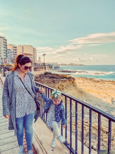 a family walks on an oceanfront boardwalk while on a vacation to Malta with a toddler