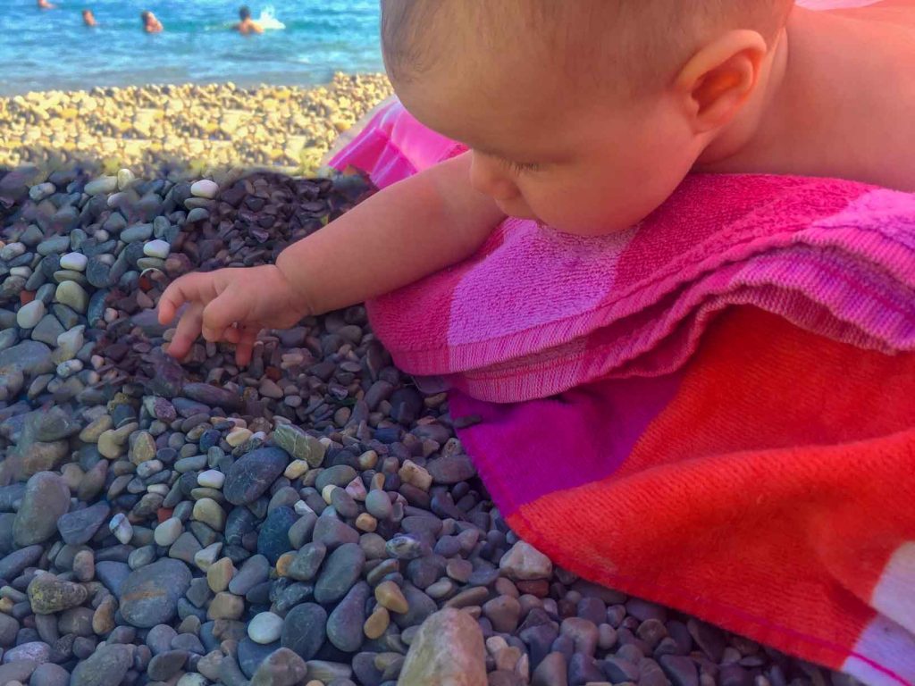 a newborn baby plays with pebbles on the beach in Nice, France - one of the best places to travel with a baby in Europe.

