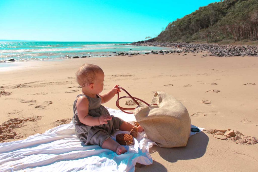 a baby plays on Noosa Beach during a family trip to Australia
