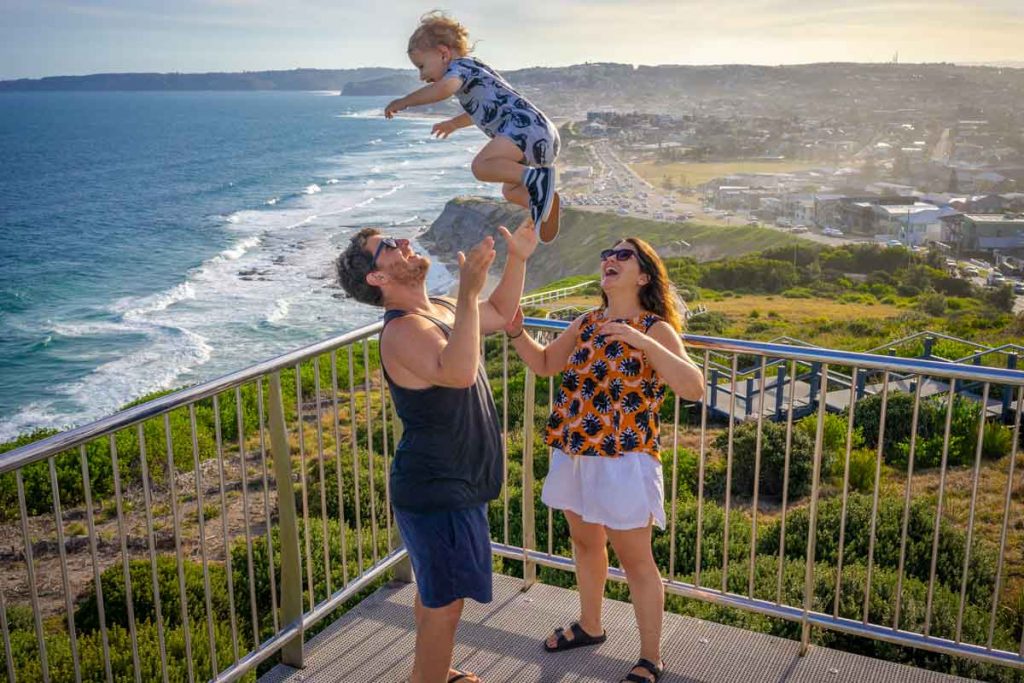 a dad throws his exhilarated toddler in the air while mom watches, during a family trip to Sydney, Australia 
