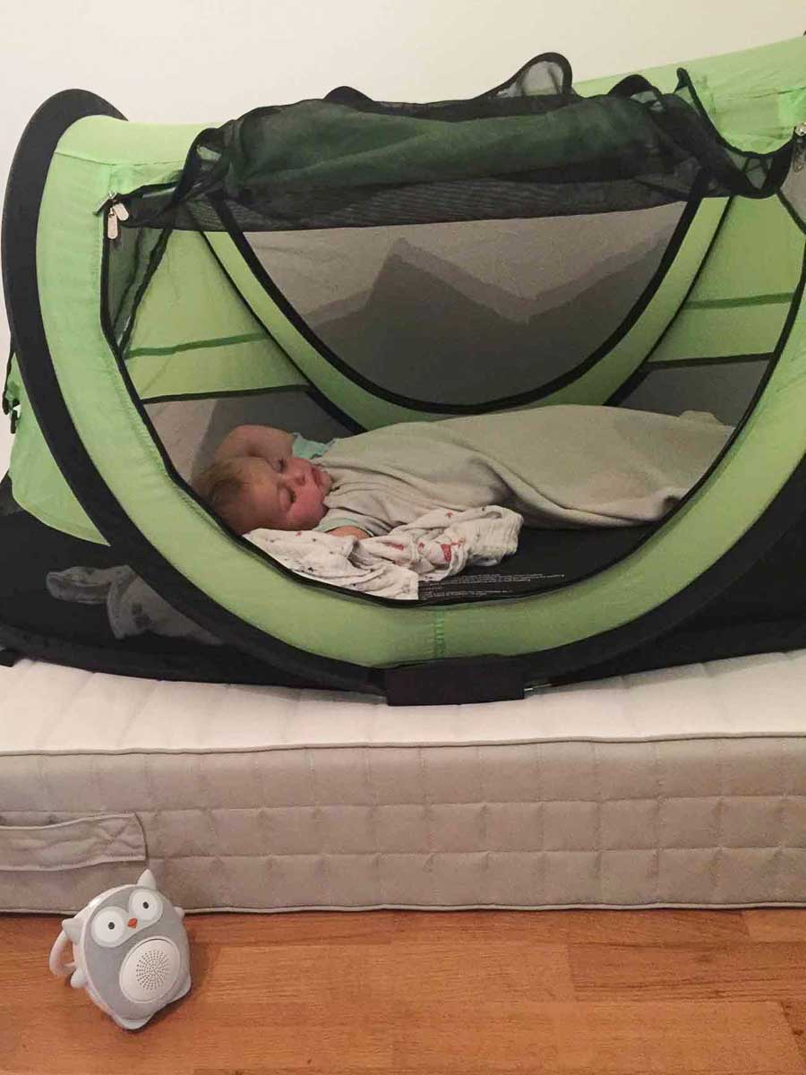 a baby from BabyCanTravel.com is sound asleep inside a toddler travel tent while listening to a white noise machine.