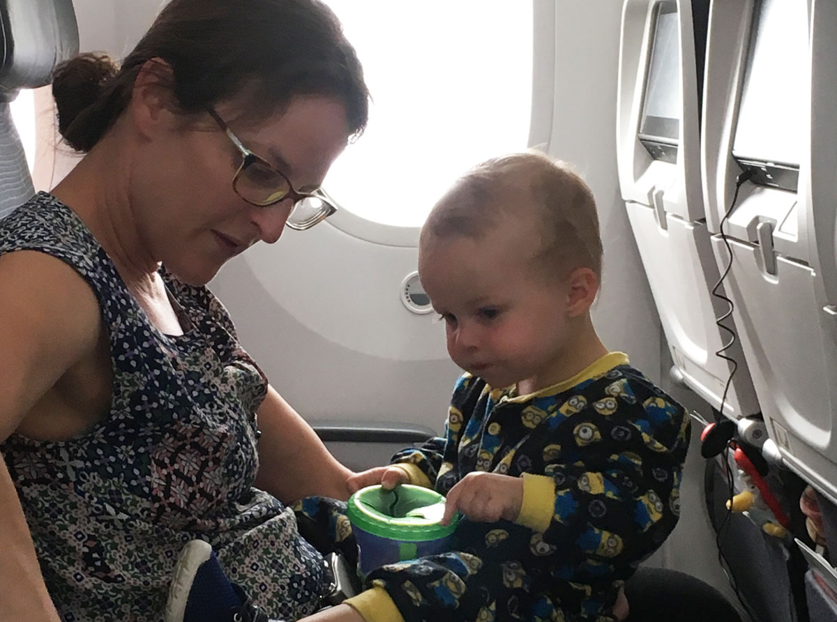 Celine Brewer, from BabyCanTravel.com, holds her baby on her lap during a family flight. Her baby eats finger foods from a spill proof snack cup.