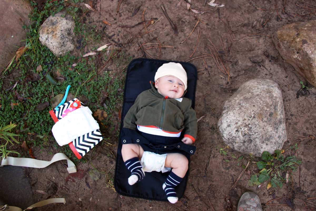 Celine Brewer, from BabyCanTravel.com, changes her baby's diaper on a portable change mat while hiking.