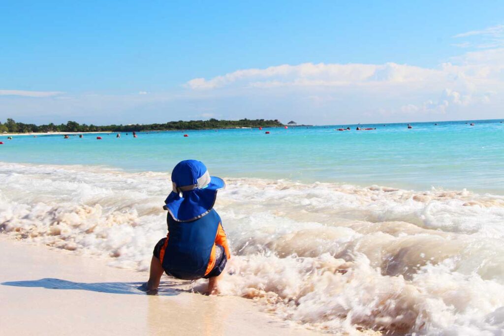 a toddler plays on the beach in Xpu-Ha, Mexico while on a tropical vacation with his family.