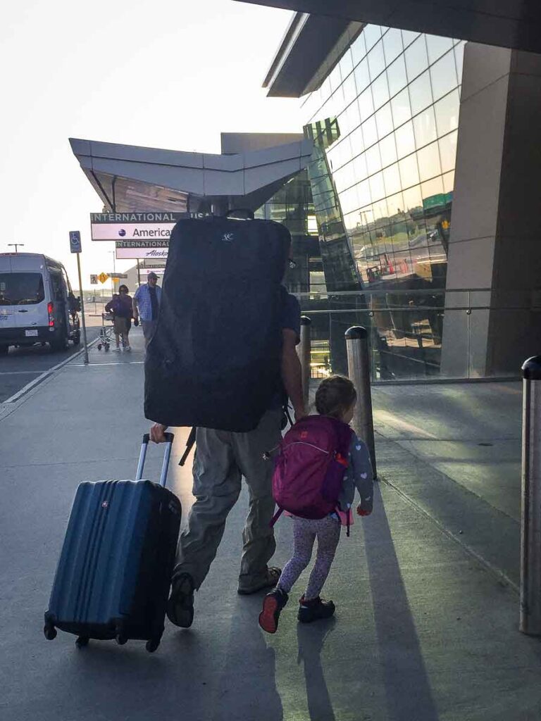 a father carries a convertible car seat in a protective travel bag on his way to checking in for a family flight