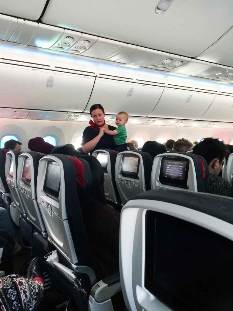 a flight attendant holds a child to help parents who are flying with a toddler