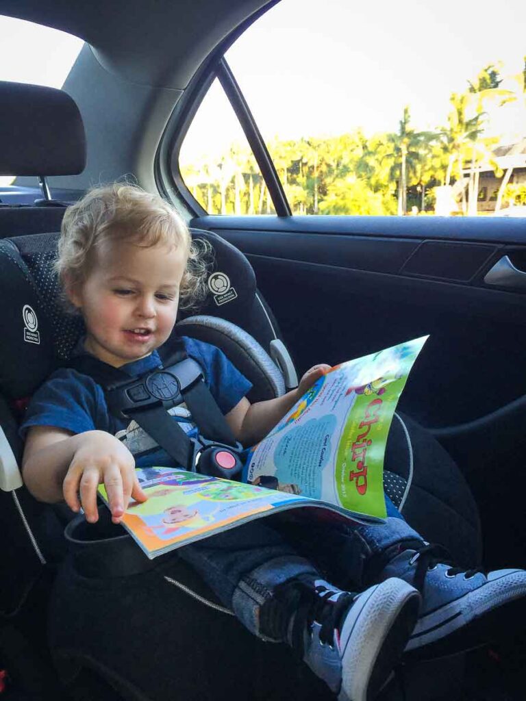 a Toddler in a front facing car seat reads chirp magazine while on a family road trip