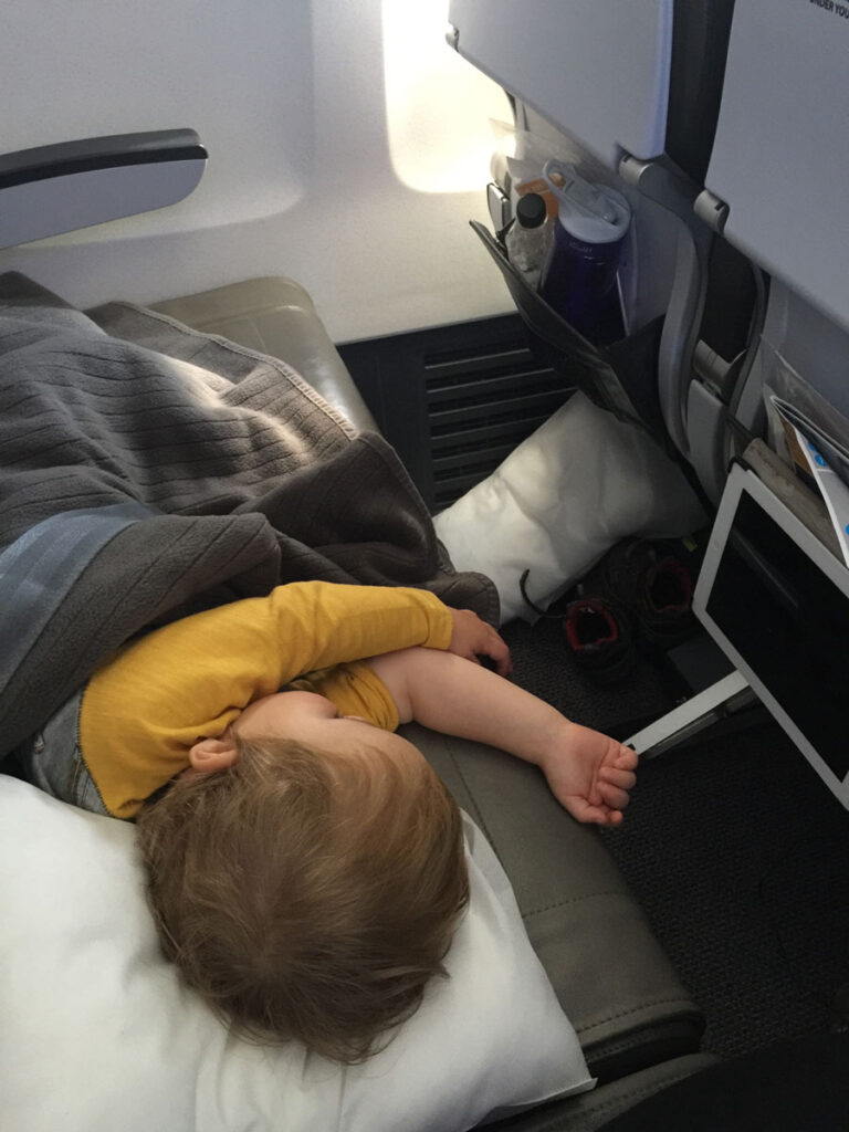 a toddler sleeping on an airplane with a pillow and blanket.