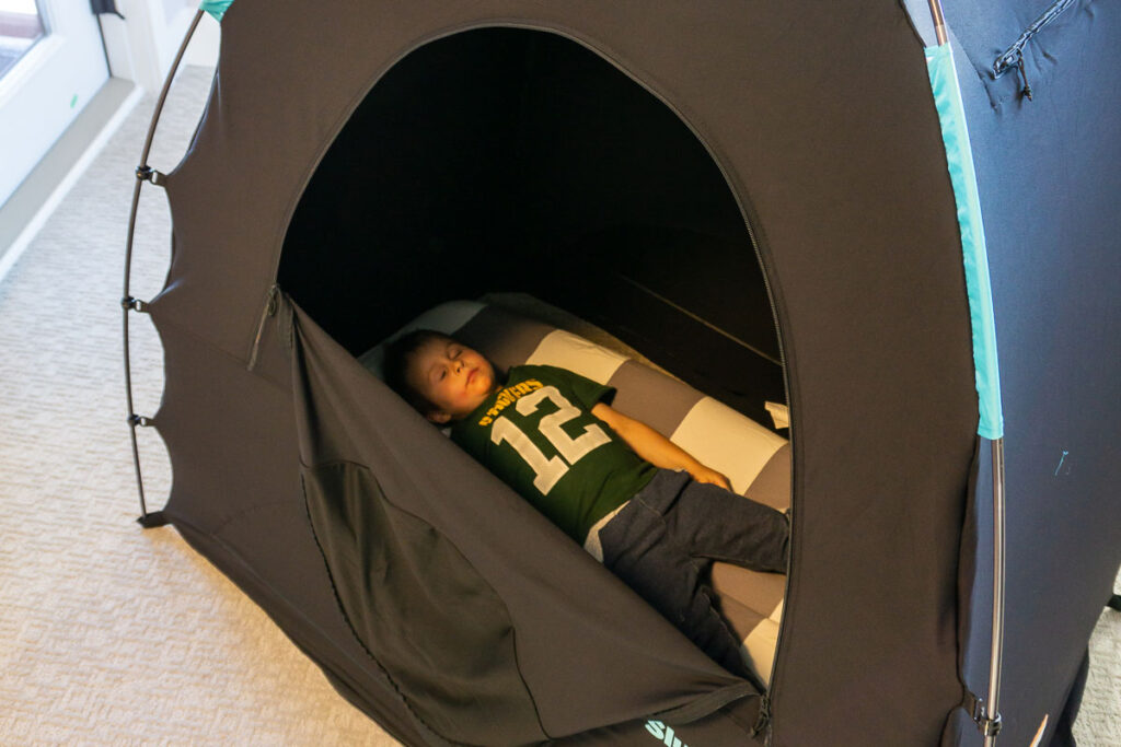 a boy from the BabyCanTravel.com family, lies on his inflatable travel bed inside a SlumberPod.