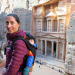 image of woman with baby in carrier on her back at Petra with the Treasury in background