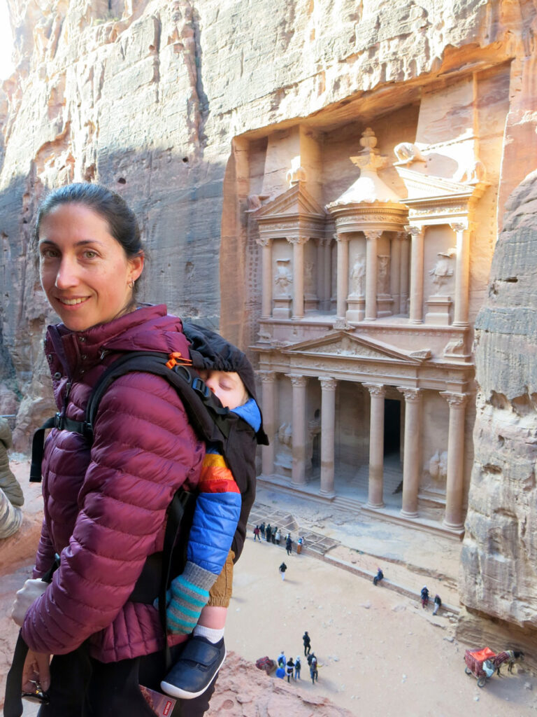 image of woman with baby in carrier on her back at Petra with the Treasury in background