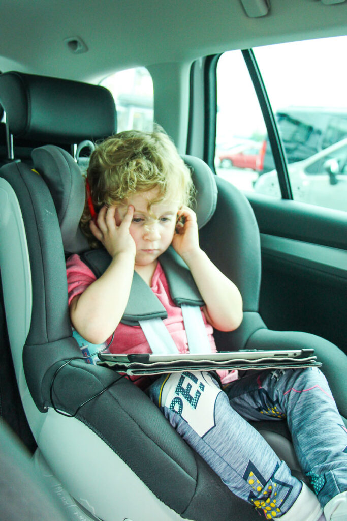 a toddler on road trip with ipad and headphones.