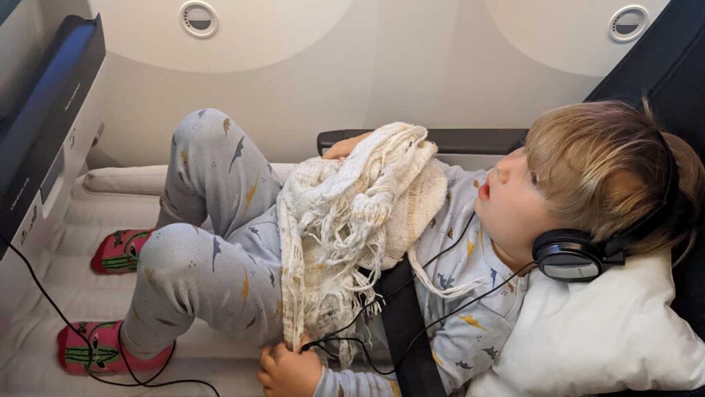 a toddler reclines on a Fly away Kids Bed while watching a movie on an airplane