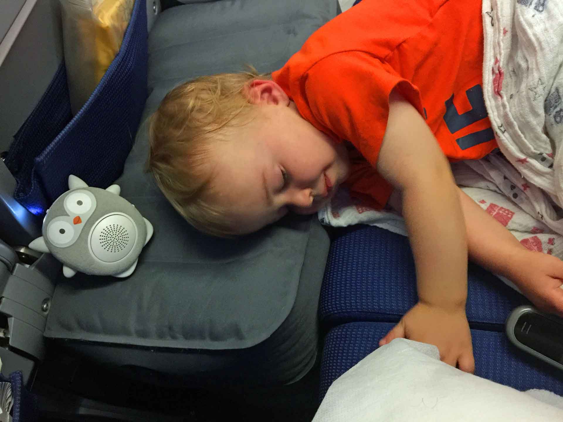 a baby from BabyCanTravel.com uses a white noise machine on a plane while sleeping on a Fly Tot travel bed.